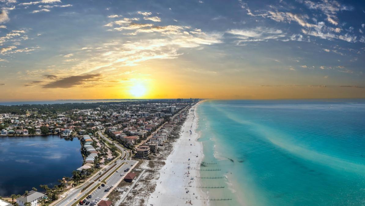 Aerial photo of Destin Florida with multiple Destin vacation rentals visible on the left, with the Gulf of Mexico on the right.